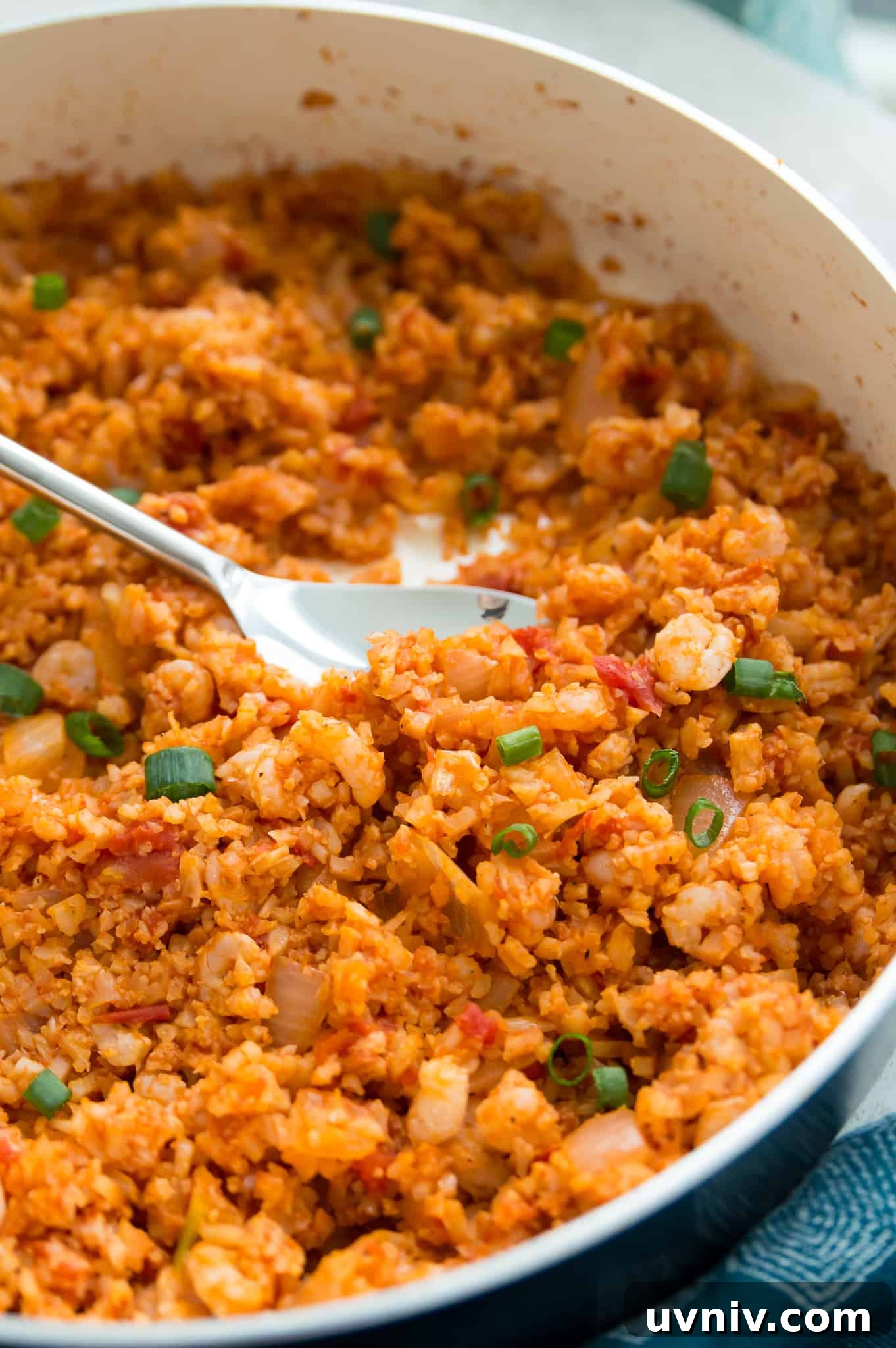 Spanish Cauliflower Rice with Shrimp — Quick Low-Carb Recipe 2 A pan of Spanish cauliflower rice with shrimp with a large spoon in it.