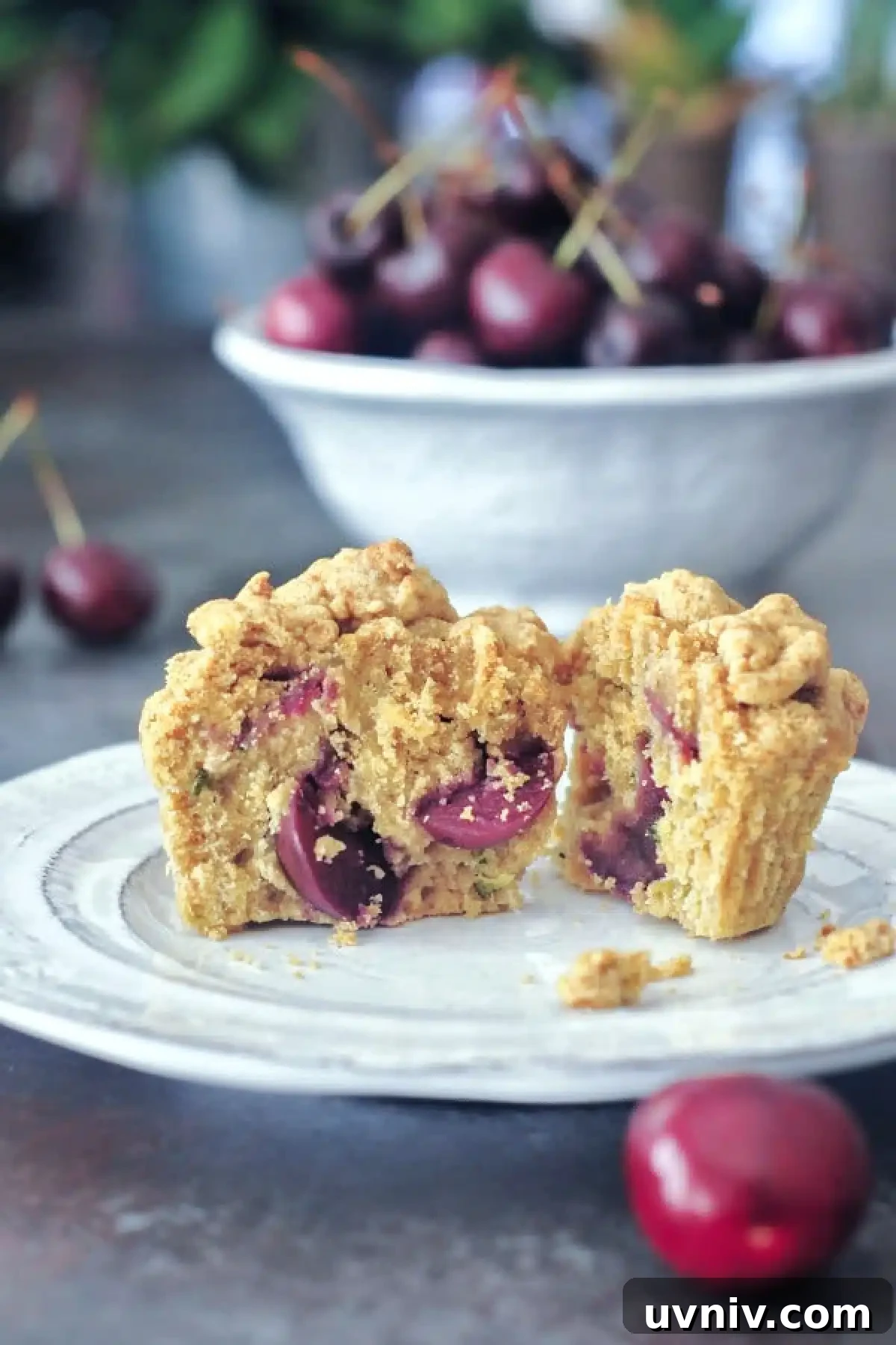 Cherry Zucchini Crumb Muffins @spabettie #glutenfree #vegan Cherry zucchini muffin sliced in half sitting on a white plate, with a bowl of cherries in background.