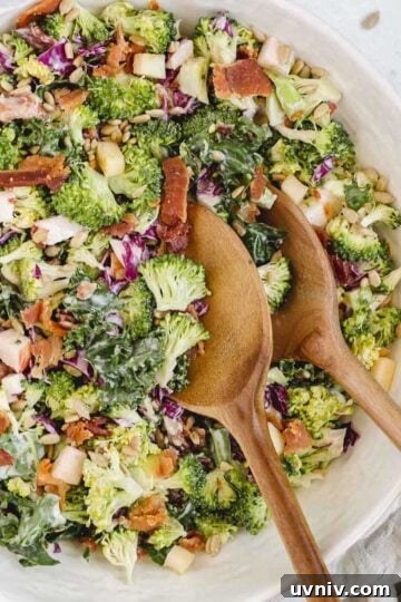 Broccoli salad with kale and red cabbage in a large serving bowl with wooden salad utensils in the bowl.