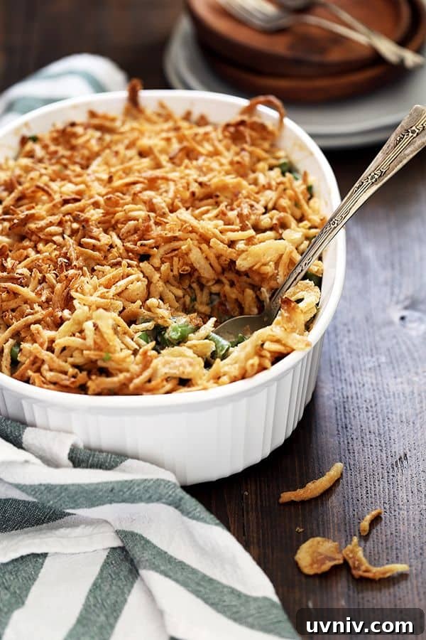 Twice the Onion Green Bean Casserole A white casserole dish holds Twice the Onion Green Bean Casserole with a spoon on a wooden surface.