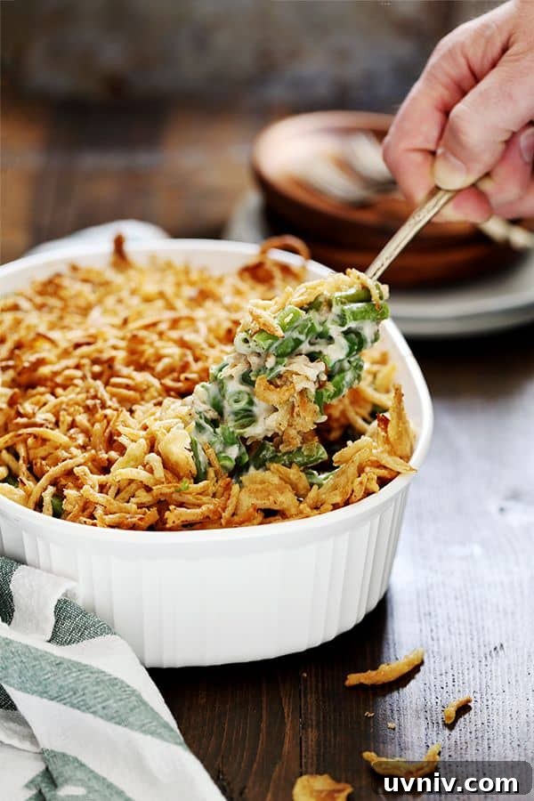 Twice the Onion Green Bean Casserole A scoop of Twice the Onion Green Bean Casserole is being lifted out of a white casserole dish.
