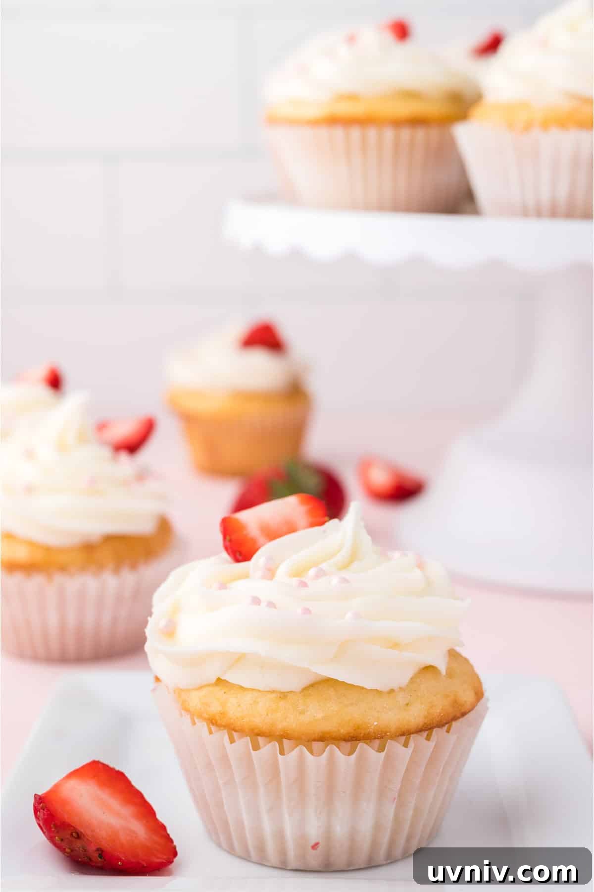 Strawberry filled cupcakes on a table with a cupcake stand in the background.