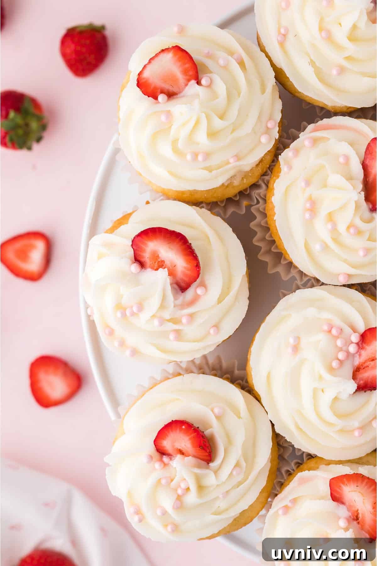 A plate of strawberry filled cupcakes with icing and strawberries for garnish.