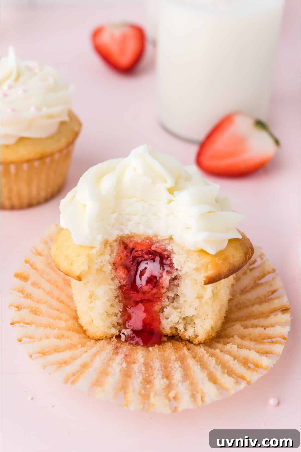 Strawberry cupcake on a paper liner with a bite missing.