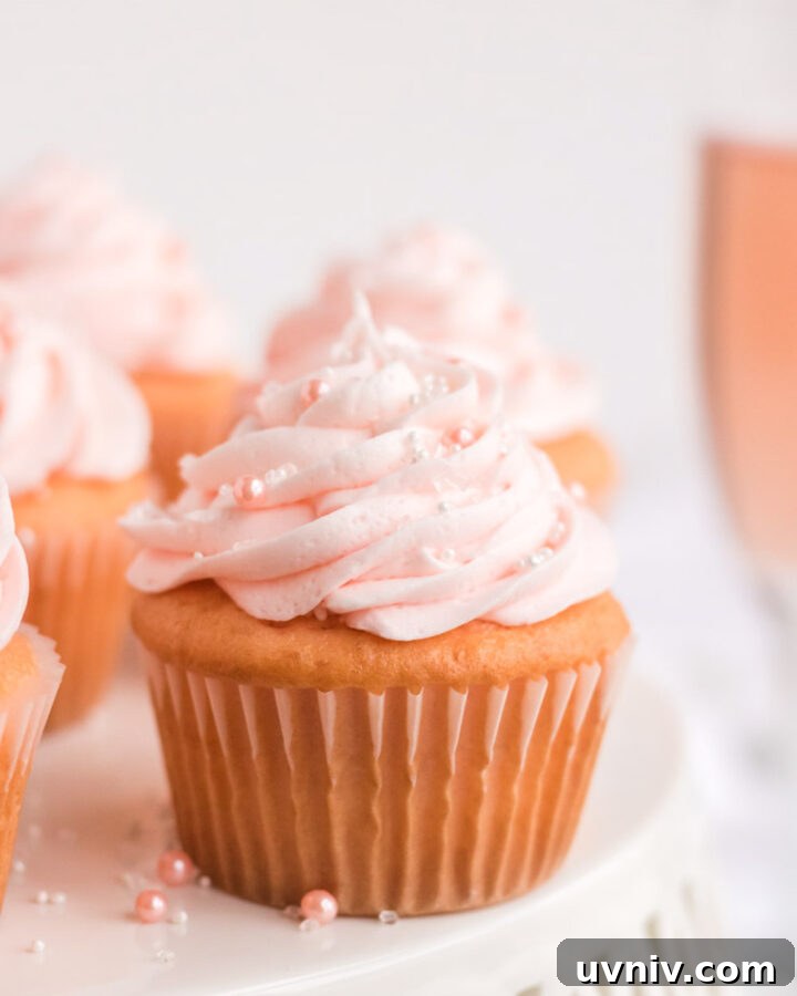 Pink champagne cupcake on a white cake stand with a glass of pink champagne behind it.