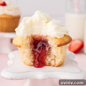 A strawberry filled cupcake with bite missing and the filing spilling out.