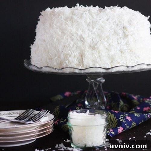 Finished coconut cake on a glass cake pedestal.