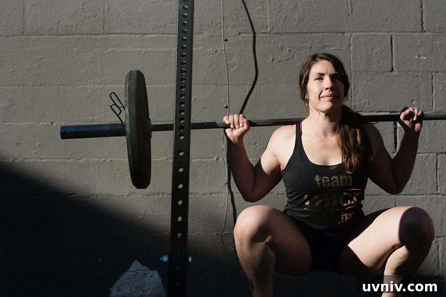 Low Energy Availability Explained: Signs, Risks, and Prevention 2 white woman with long brown wavy hair in a ponytail wearing a black tank top and black shorts holds onto a barbell does a barbell squat - low energy availability