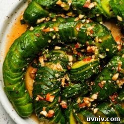 Sliced cucumber salad with chili, garlic, and sesame seeds on a white plate.