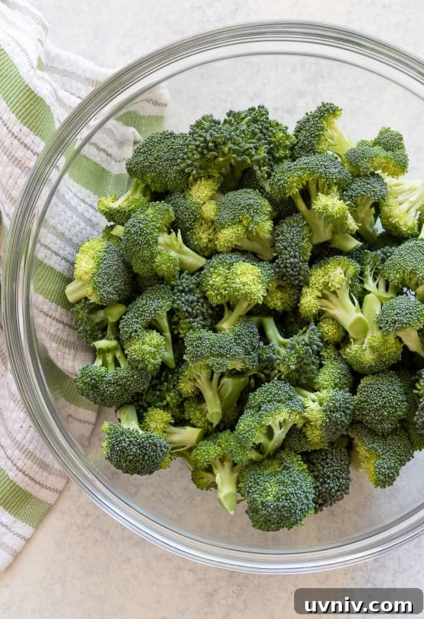 Raw broccoli florets in a glass bowl with a green striped towel.