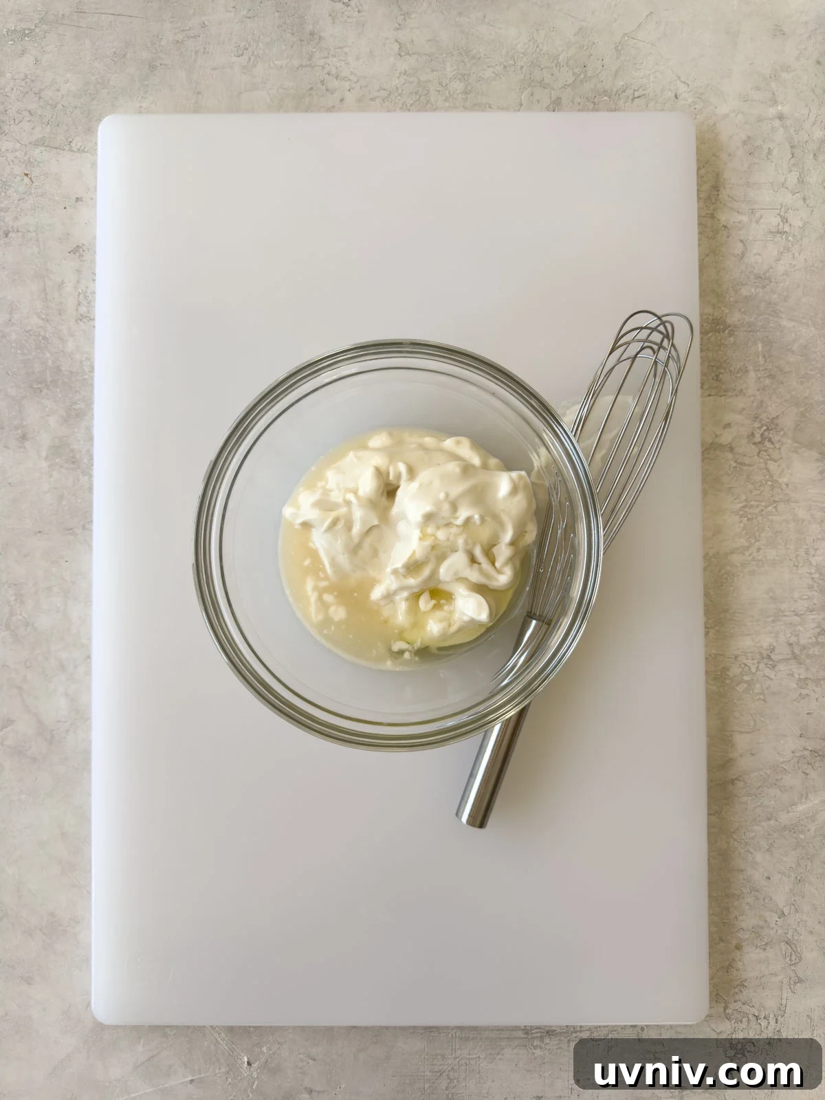 Mayonnaise, vinegar, and honey in a glass bowl with a stainless steel whisk.