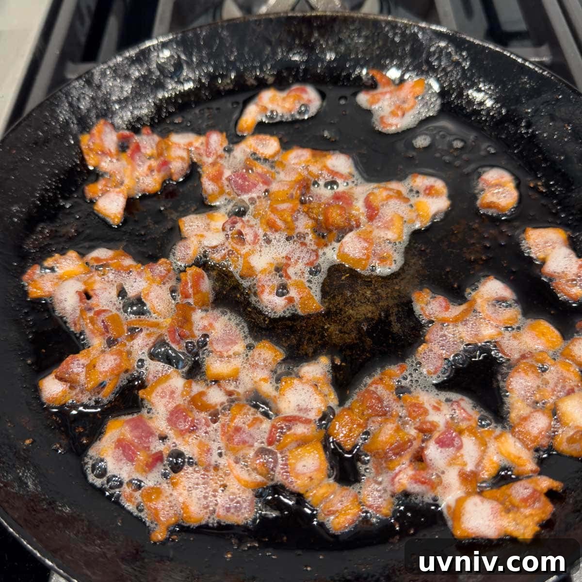 Cooking bacon pieces in a black iron skillet golden brown.