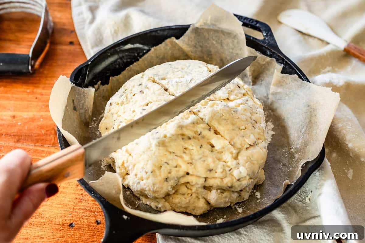 Authentic Irish Soda Bread Recipe You Can Make at Home 13 Slicing divots in the top of Irish soda bread dough before baking with bread knife in cast iron skillet.