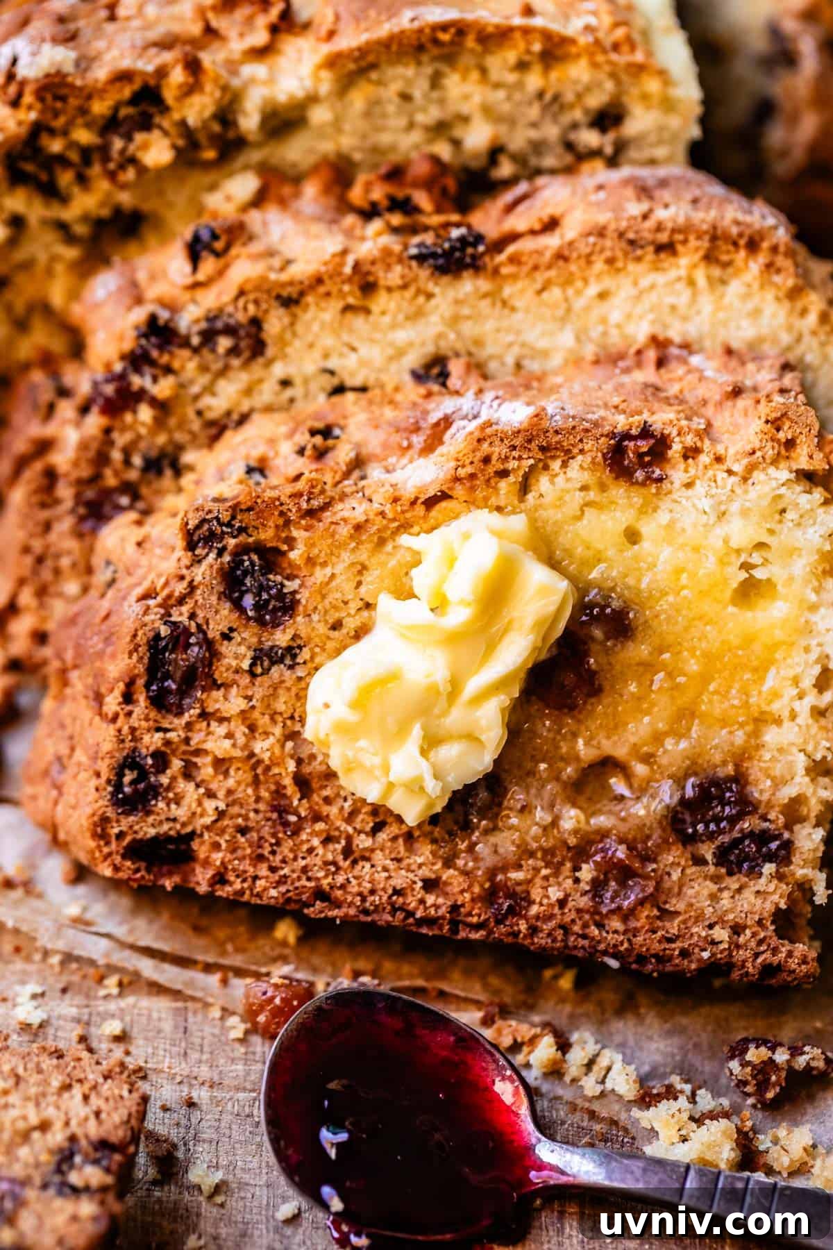 Authentic Irish Soda Bread Recipe You Can Make at Home 6 Irish soda bread slices leaning atop one another on cutting board with pat of butter on top and small spoon with blackberry jam.