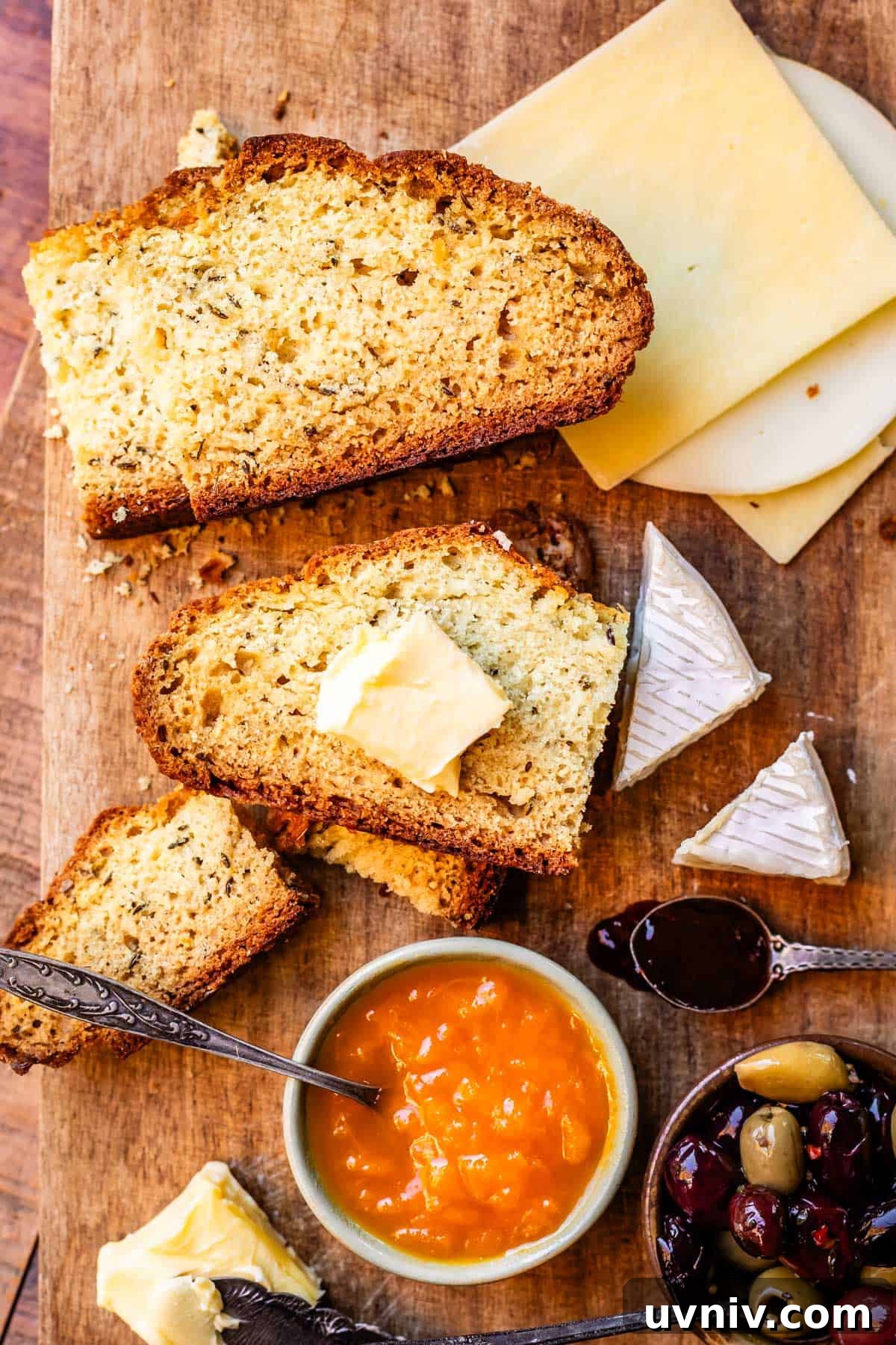 Authentic Irish Soda Bread Recipe You Can Make at Home 8 Delicious spread of bread board with Irish soda bread, apricot jam, cheeses, and olives on a wooden cutting board.