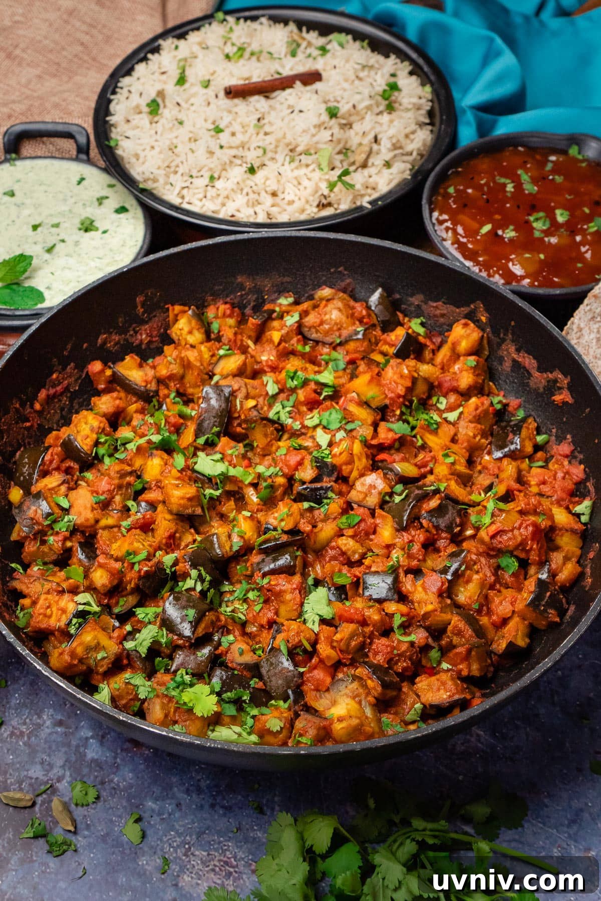 Spiced Brinjal Bhaji: Authentic Indian Eggplant Curry Recipe 8 Brinjal Bhaji Indian Curry in a pan with jeera rice, mint raita and mango chutney on the side