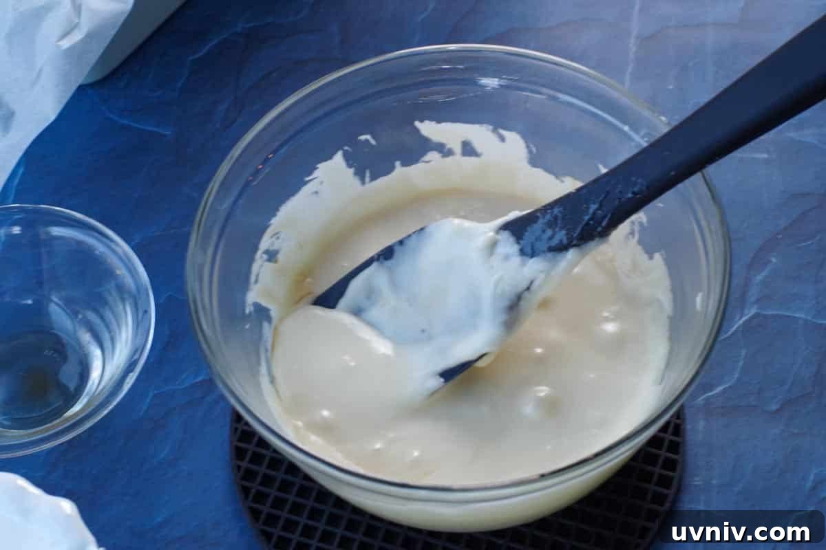 Root Beer Float Fudge Recipe: Creamy Soda-Infused Candy 11 ⅓ of mixture poured into glass bowl, with vanilla added and black spatula in bowl