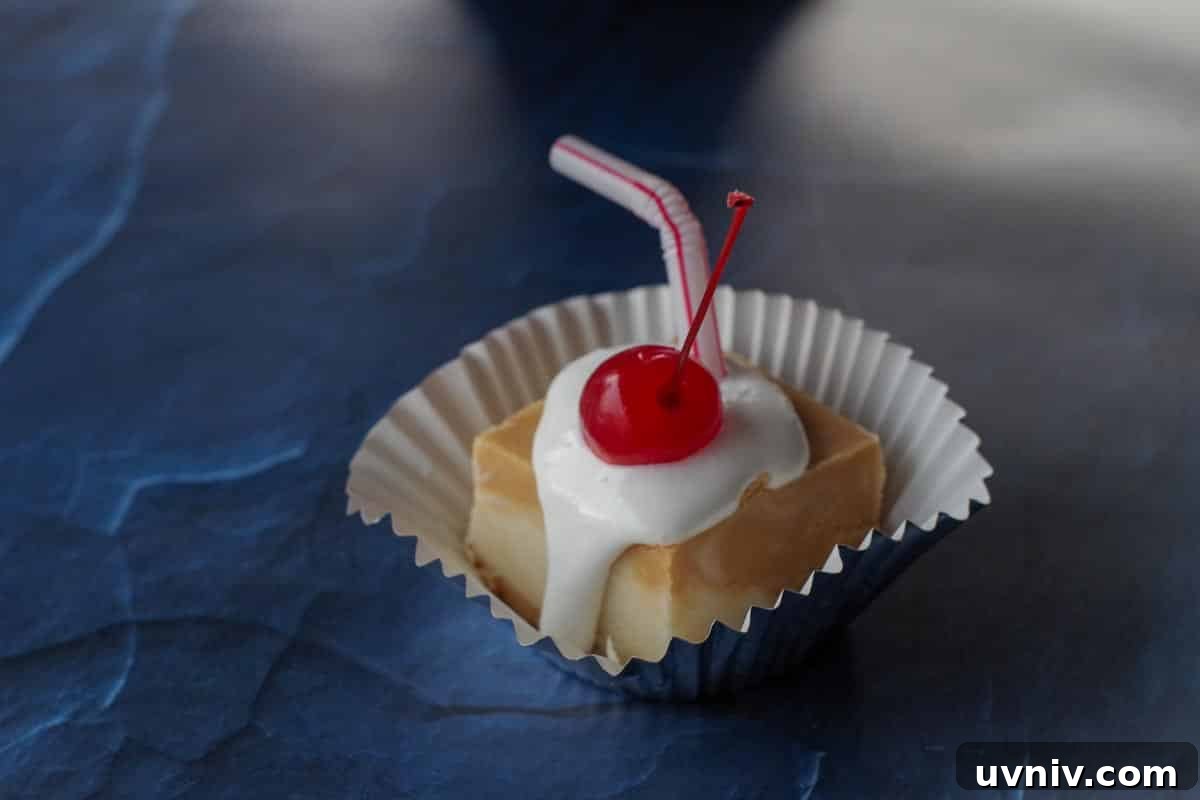 Root Beer Float Fudge Recipe: Creamy Soda-Infused Candy 5 a piece a root beer float fudge on a cupcake liner, with marshmallow fluff and cherry, with a straw in it on a blue surface