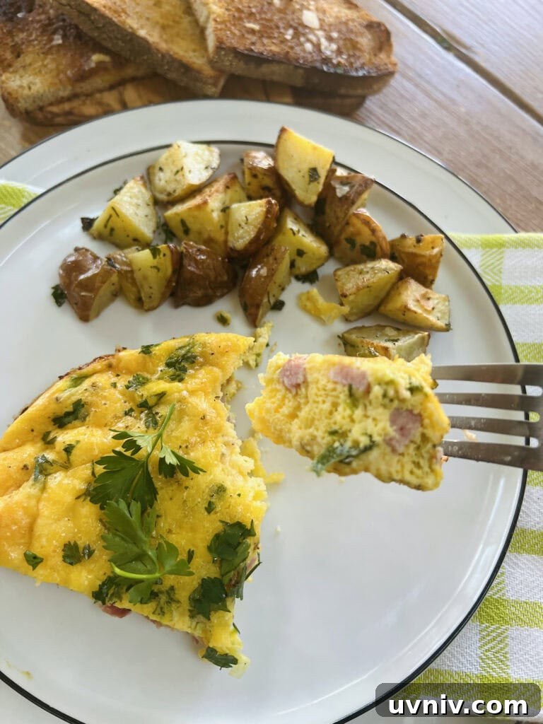 Close up of piece of cheese and ham frittata on fork with the rest of frittata slice and roasted potatoes in background.