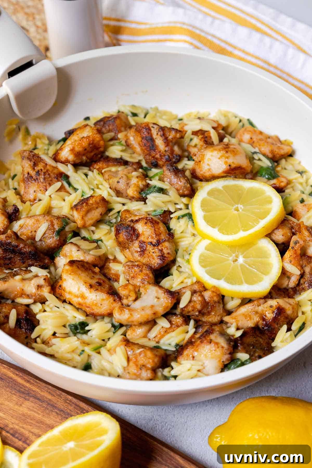 Seasoned diced chicken thighs in a large skillet with orzo, spinach, and lemon slices.