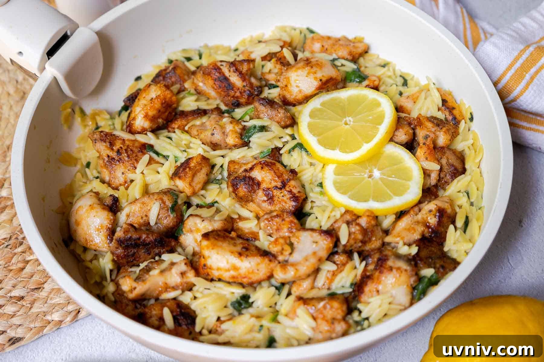 Seasoned diced chicken in a skillet with orzo, chopped baby spinach, and lemon slices.