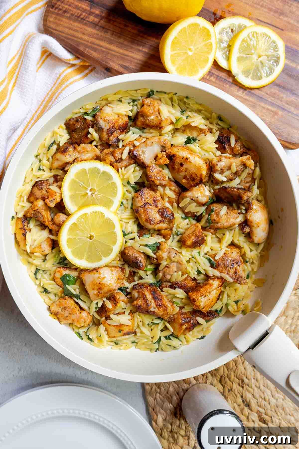 Seasoned diced chicken in a skillet with orzo, chopped baby spinach, and lemon slices.