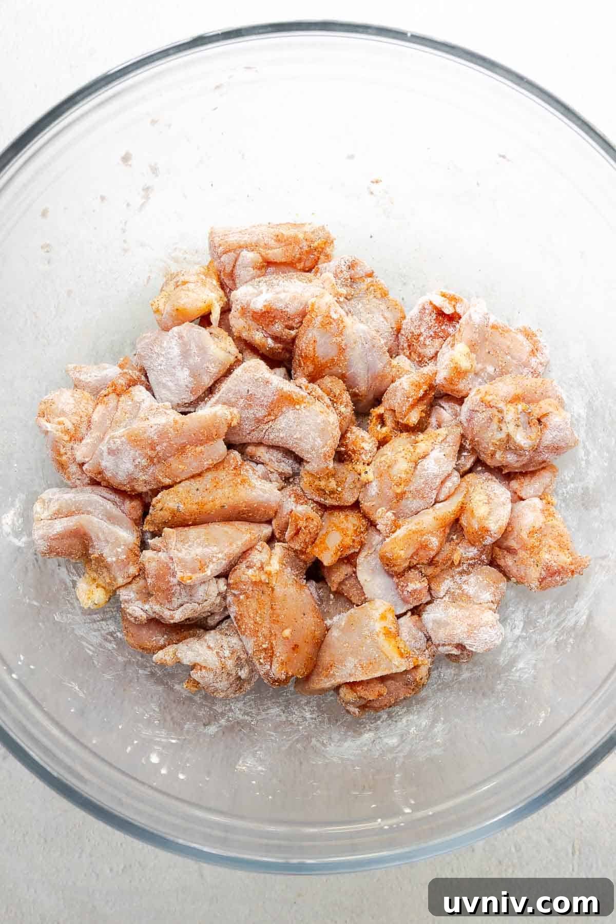 Diced chicken thighs coated in seasoning and cornstarch in a mixing bowl.