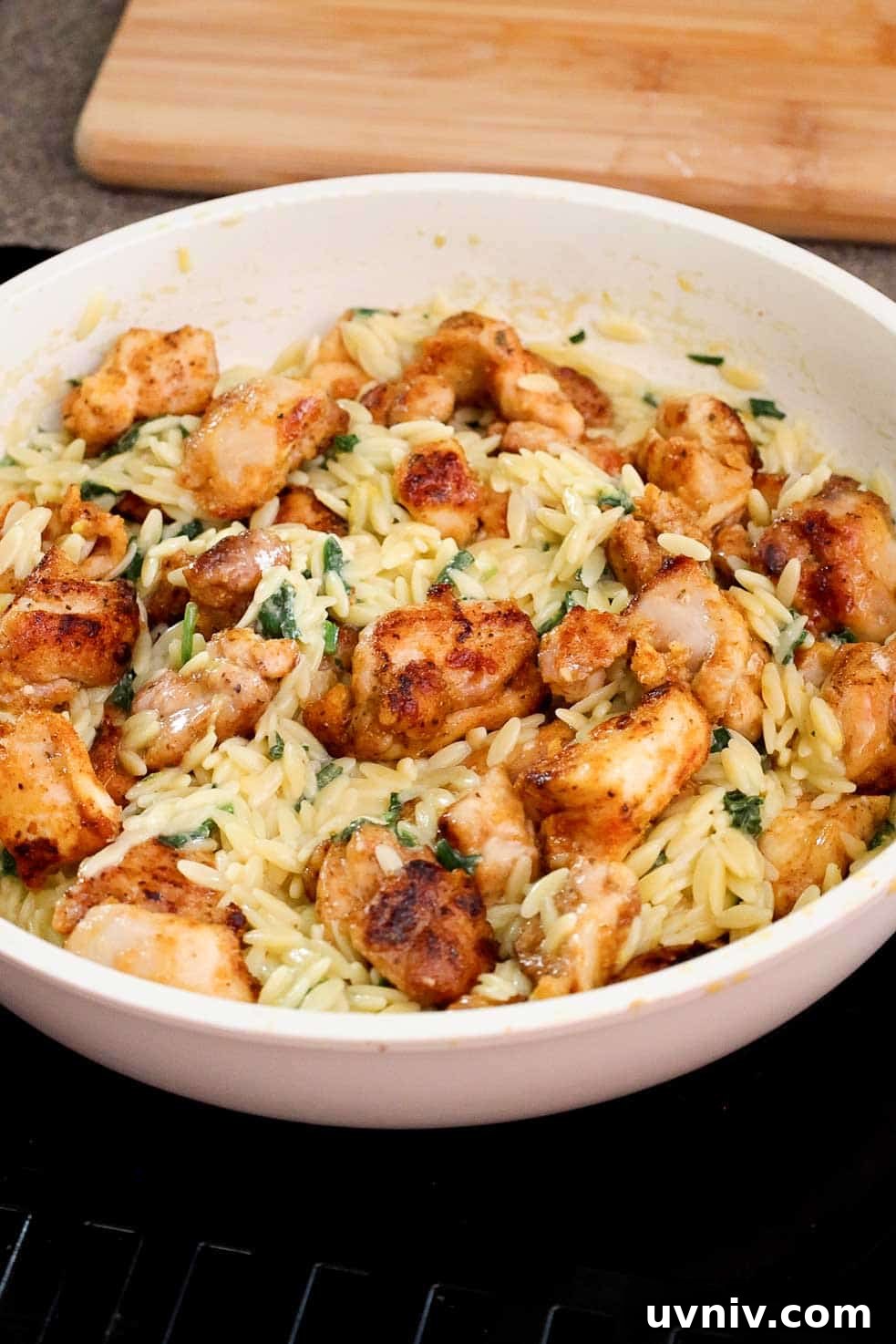 Cooked diced chicken thighs tossed with lemon orzo in a large skillet.