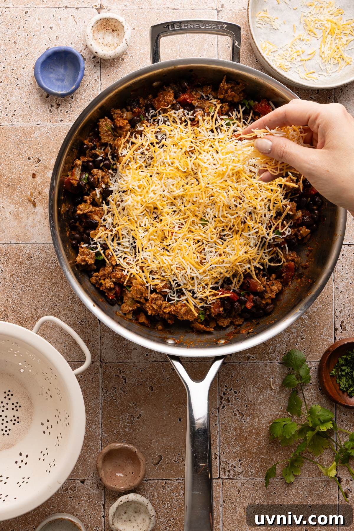 Cheesy Turkey Taco Skillet Dinner — One-Pan Weeknight Meal 11 A person's hand sprinkling shredded cheddar cheese over a turkey taco skillet before baking it