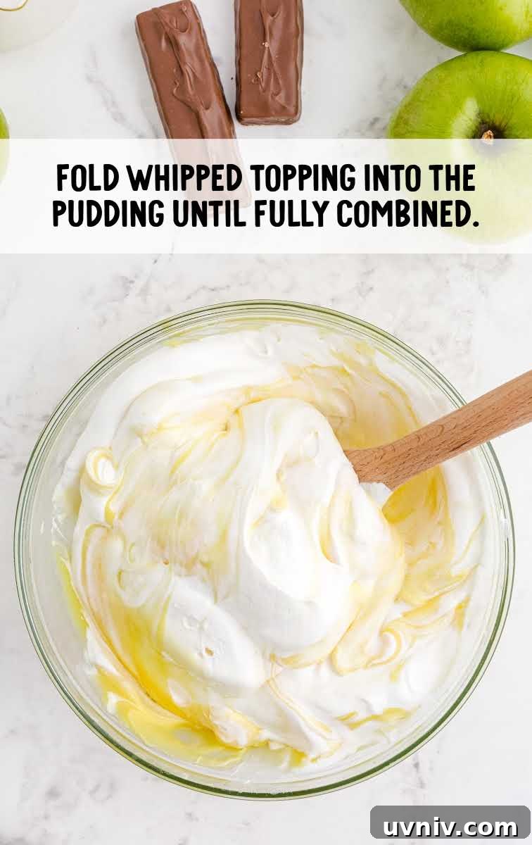 Snickers Salad Recipe: Creamy Dessert Salad with Chocolate & Peanut Butter 4 cool whip being combined into the ingredients in a bowl