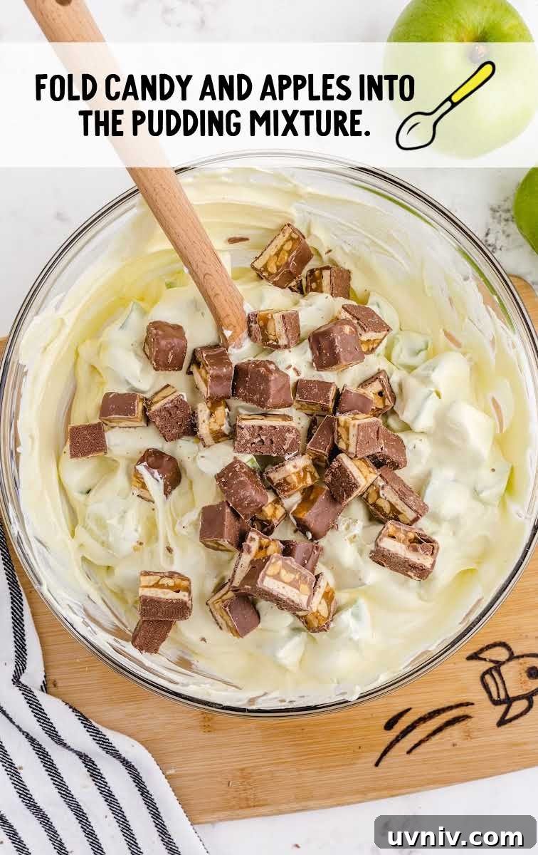 Snickers Salad Recipe: Creamy Dessert Salad with Chocolate & Peanut Butter 7 snickers and apples being added to the pudding mixture in a bowl