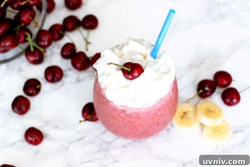 Creamy Cherry Banana Smoothie Recipe for Quick Energy 5 A close up of a glass filled with cherry smoothie and whipped cream on a white table.