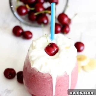 Creamy Cherry Banana Smoothie Recipe for Quick Energy 6 A close up of glass filled with smoothie topped with whipped cream and a cherry.