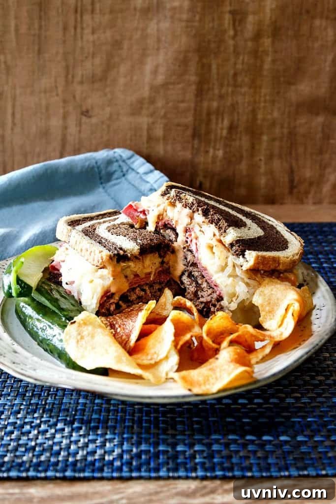 Smashed Reuben Burger with smoky Russian dressing A plate with a burger made on rye bread, cut in half, with pickle spears and potato chips.
