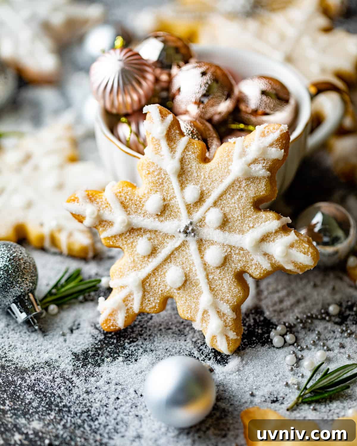 How to Make Perfect Snowflake Sugar Cookies for Winter Parties 2 a snowflake cookie standing up on a table with christmas bulbs around the cookie.