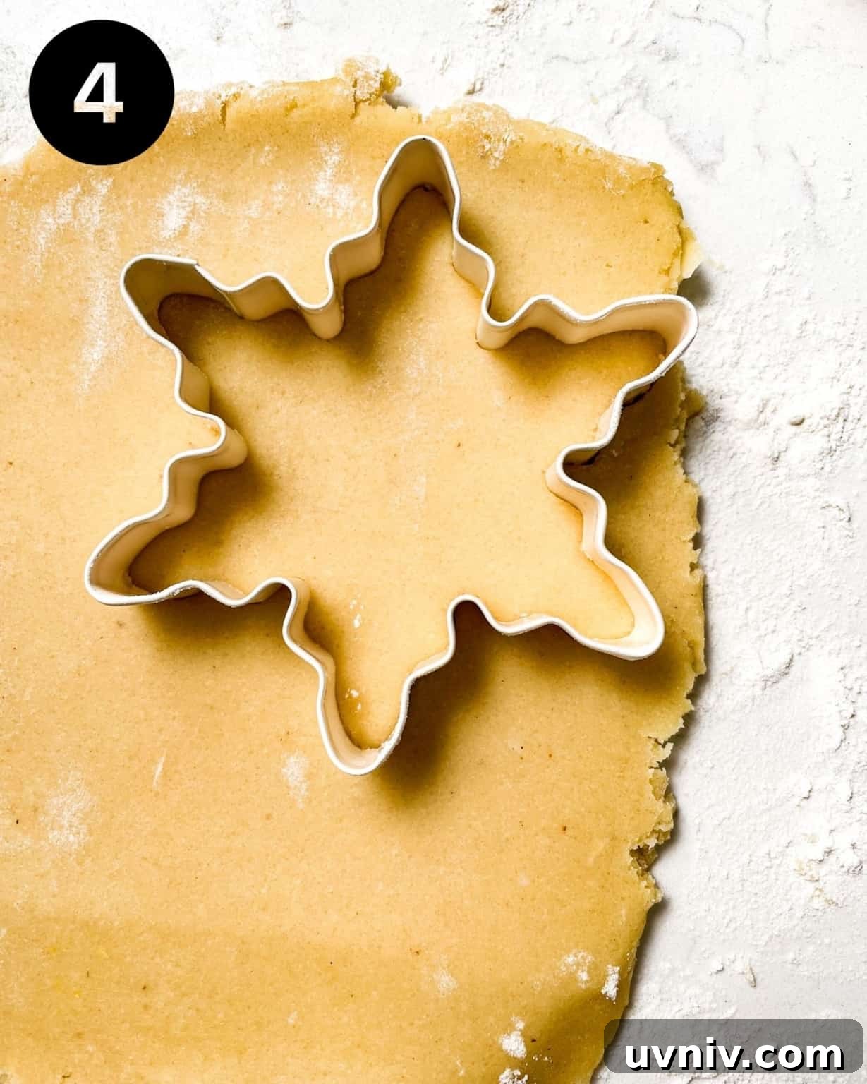 How to Make Perfect Snowflake Sugar Cookies for Winter Parties 7 cookie dough rolled out onto a surface with a snowflake cookie cutter pressed into the dough.