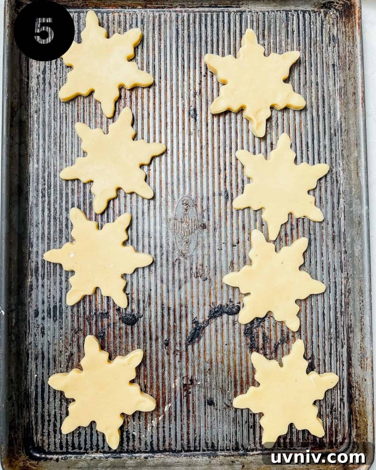 How to Make Perfect Snowflake Sugar Cookies for Winter Parties 8 snowflake cookies on a baking sheet.