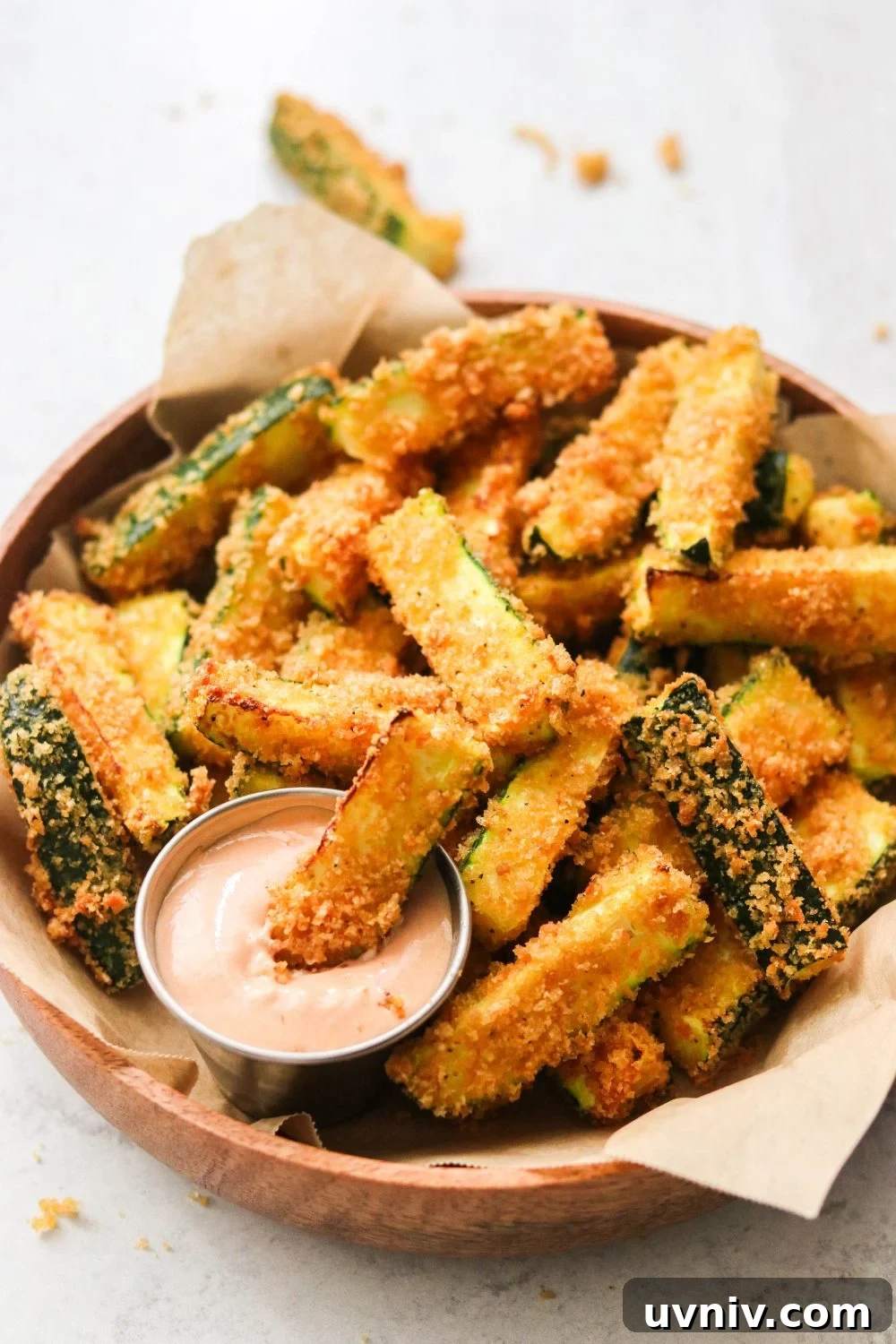 air fryer zucchini fries in a brown bowl next to a small container of dipping sauce