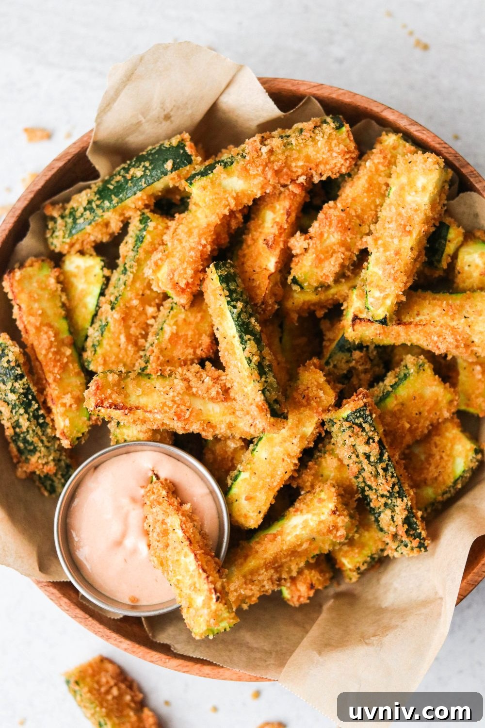 an overhead shot of air fryer zucchini fries in a brown bowl with one dipping into a sauce.