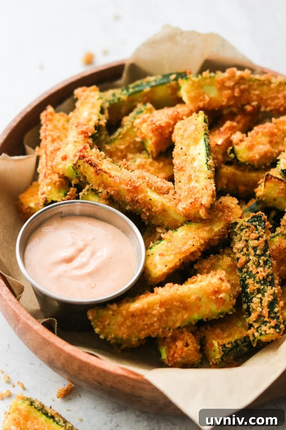 a side view of zucchini sticks fried with pork panko with a silver bowl of dipping sauce nearby.
