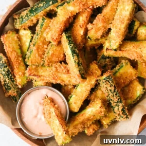 an overhead shot of air fryer zucchini fries in a brown bowl with one dipping into a sauce.