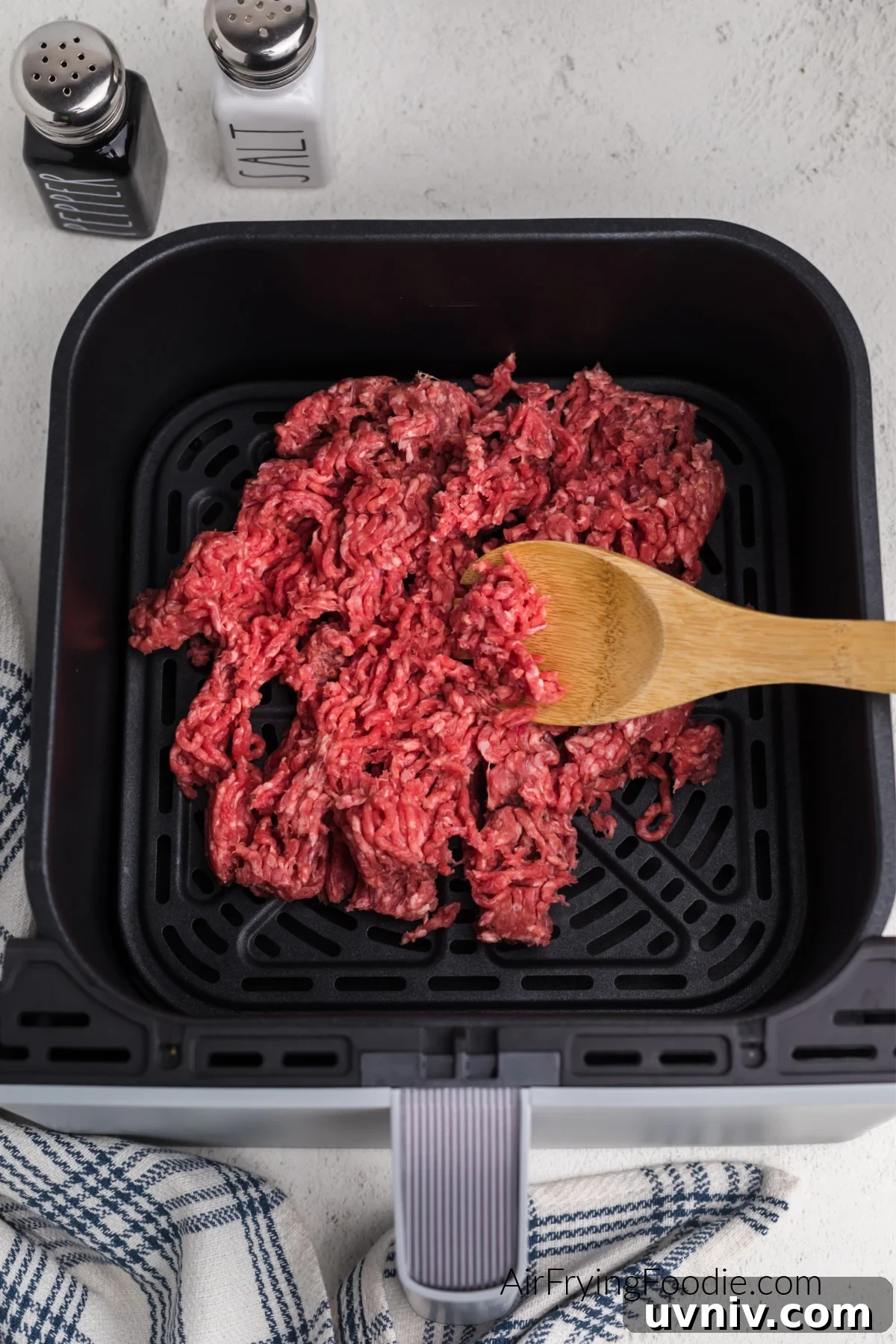 Ground beef in basket of air fryer broken up and ready to be cooked.