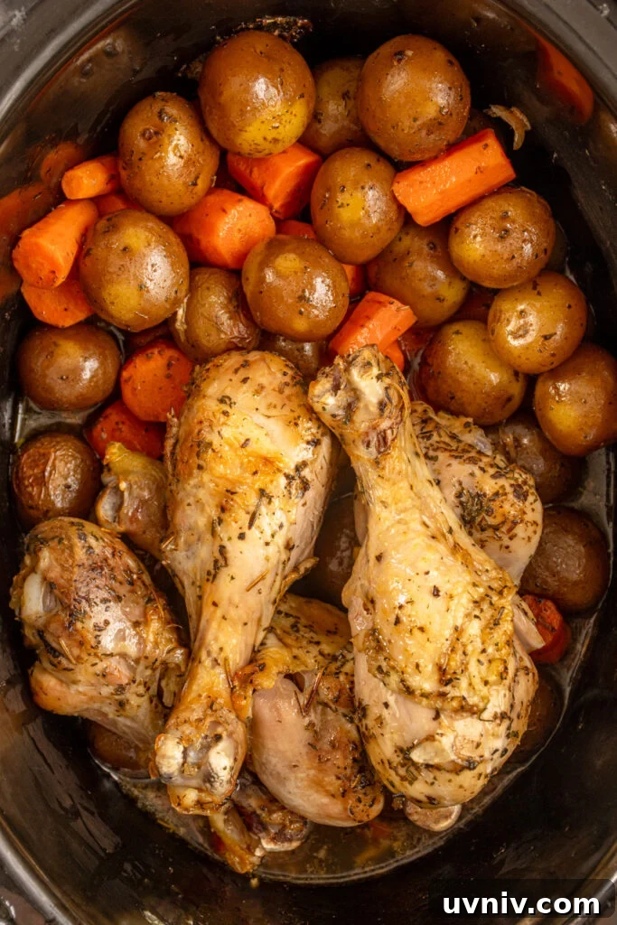 Slow Cooker Chicken Legs with Crispy Potatoes Recipe 2 A black crockpot with cooked carrots, potatoes, and chicken legs.