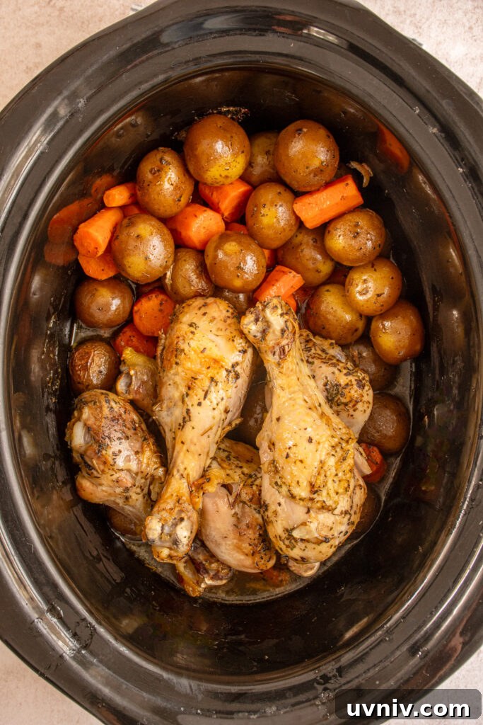 Slow Cooker Chicken Legs with Crispy Potatoes Recipe 12 A black crockpot filled with cooked carrots and baby potatoes with chicken legs.