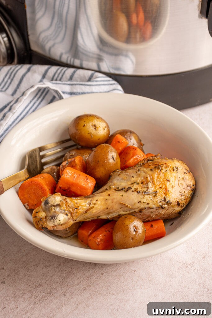 Slow Cooker Chicken Legs with Crispy Potatoes Recipe 13 A chicken leg with carrots and baby potatoes in a white bowl with a fork.