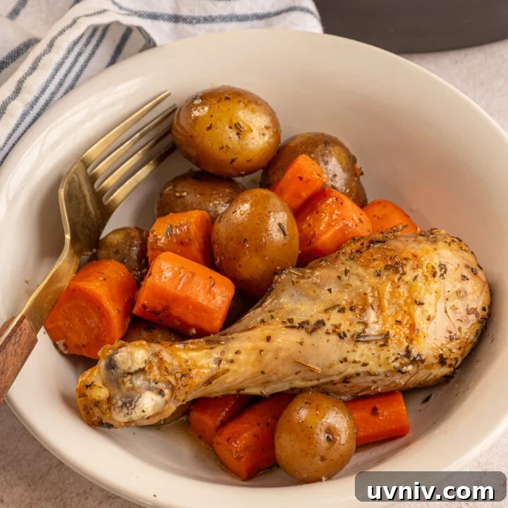 A white bowl with cooked potatoes and carrots with a chicken leg.