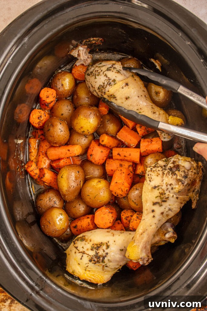 Slow Cooker Chicken Legs with Crispy Potatoes Recipe 10 Taking a cooked chicken leg out of the crockpot showing the cooked vegetables underneath.