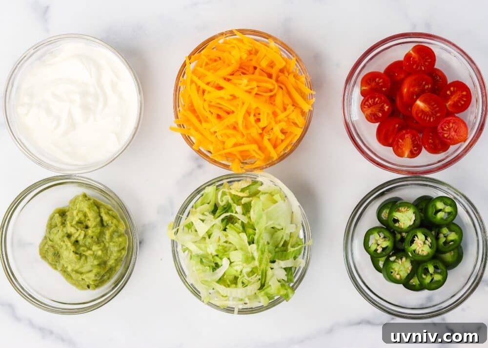Toppings ready to be assembled for keto taco bowls including lettuce, sliced cherry tomatoes, shredded cheddar cheese, guacamole, sour cream, and sliced jalapenos