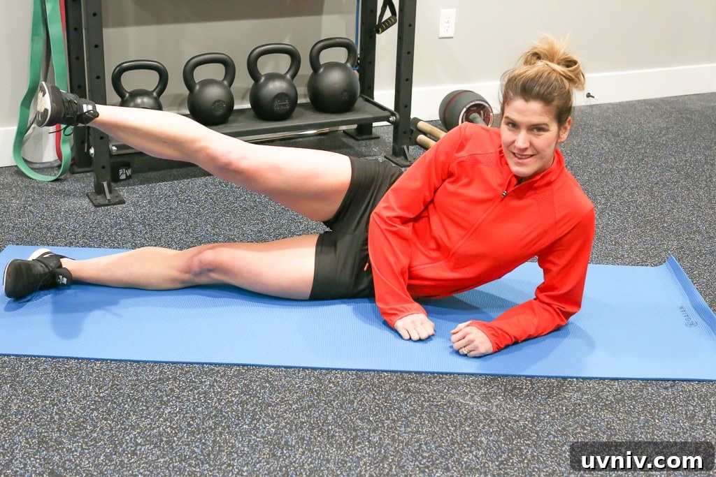 Effective At-Home Leg Workout Routine for Strength and Tone 7 Maryea Flaherty in a red jacket and black shorts laying on her side on a blue mat with one leg extended
