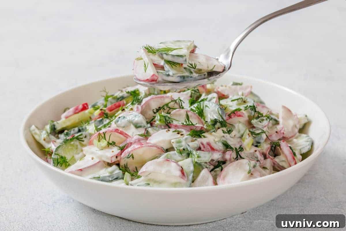 A bowl of Creamy Radish Salad garnished with dill, with a spoon lifting a portion above the bowl.